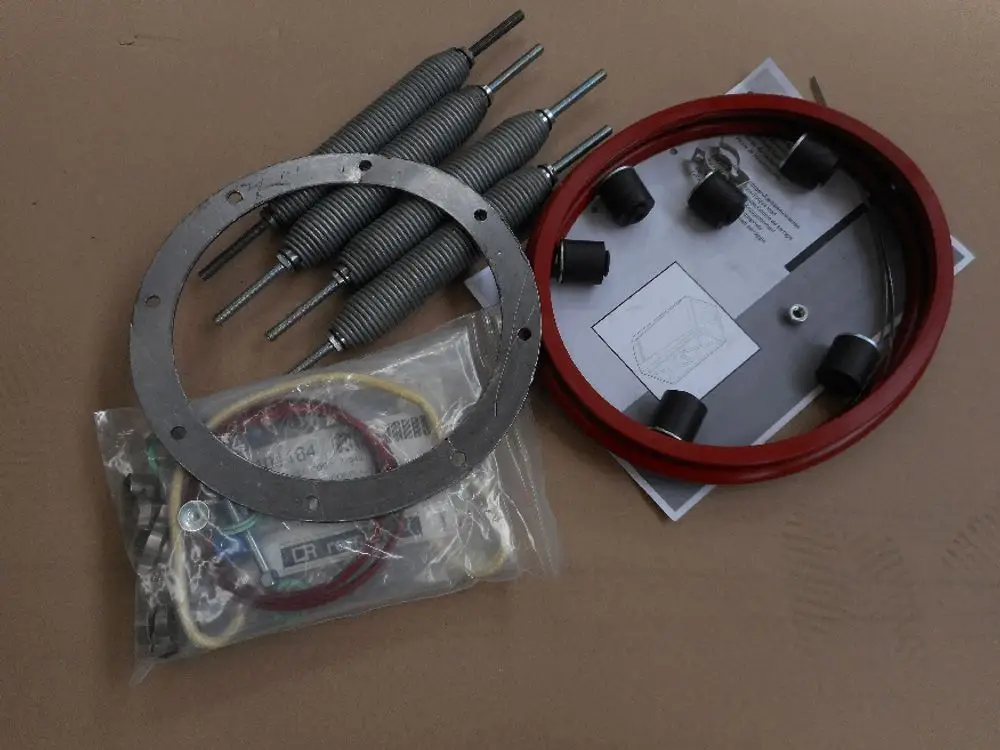 Remeha Montagezubehör bestehend aus Federn, einer Metallplatte, einem roten Ring und einem Beutel mit weiteren Elementen, auf einem neutralen Untergrund angeordnet.